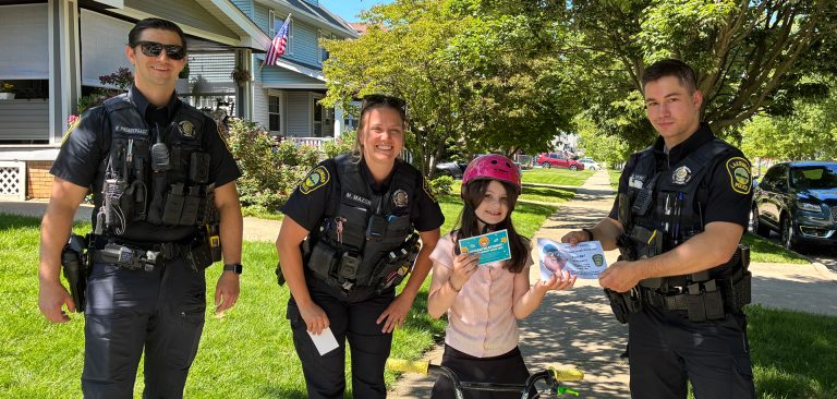 Three Lakewood Police officers pose with a young girl wearing a helmet on her bike. She is holding a certificate as part of the "Caught Being Safe" program.