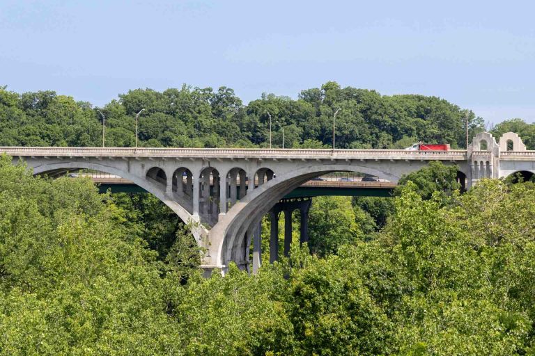 The Hilliard Road Bridge with trees of the metroparks in the foreground. The bridge is an old concrete arch bridge.