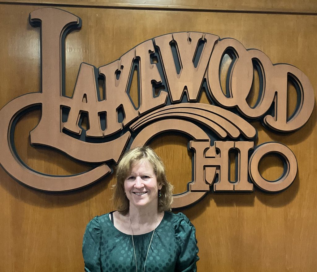 Mary Davern in front of a wood Lakewood Ohio logo.
